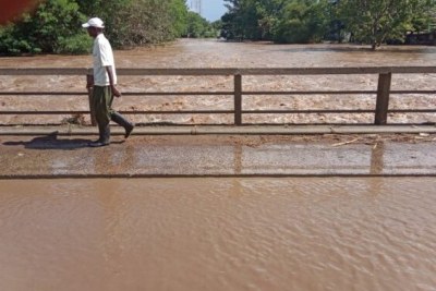 A pedestrian braves rising waters on the Ahero bridge as River Nyando overflows, highlighting the ongoing flood crisis in Kisumu County.